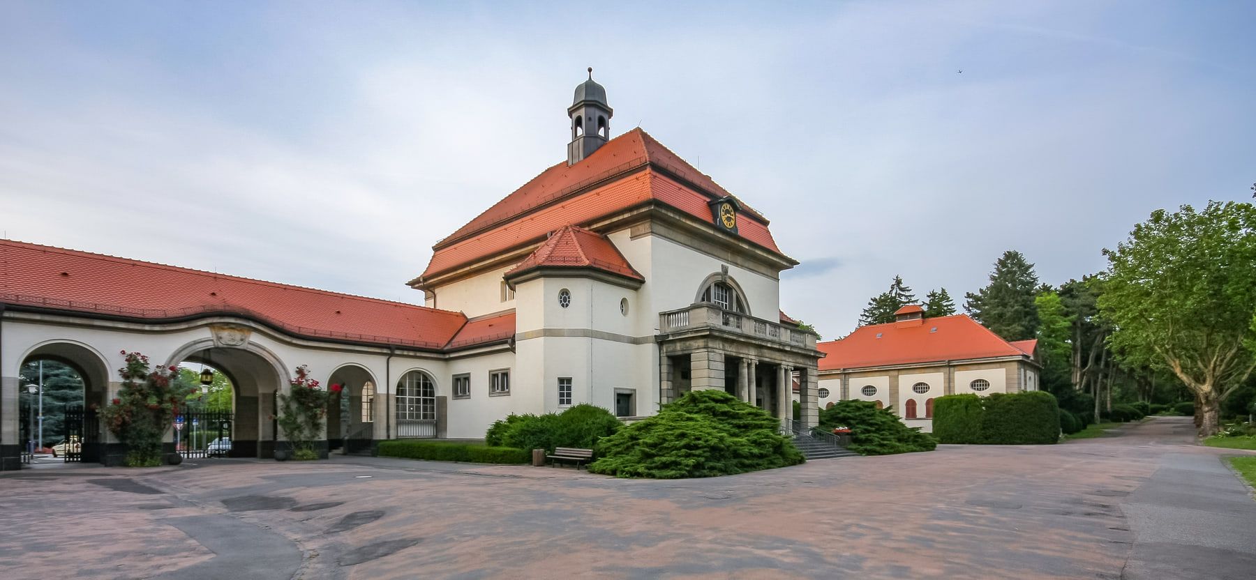 Weitwinkelansicht der historischen Kapellenanlage mit roten Walmdächern, Arkadengang und begrüntem Vorplatz auf Südfriedhof Wiesbaden