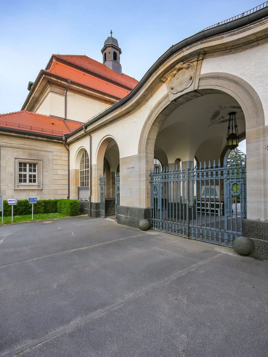 Detail des Arkadeneingangs mit ornamentiertem Rundbogen, Metalltor und Kapellenturm auf Südfriedhof Wiesbaden